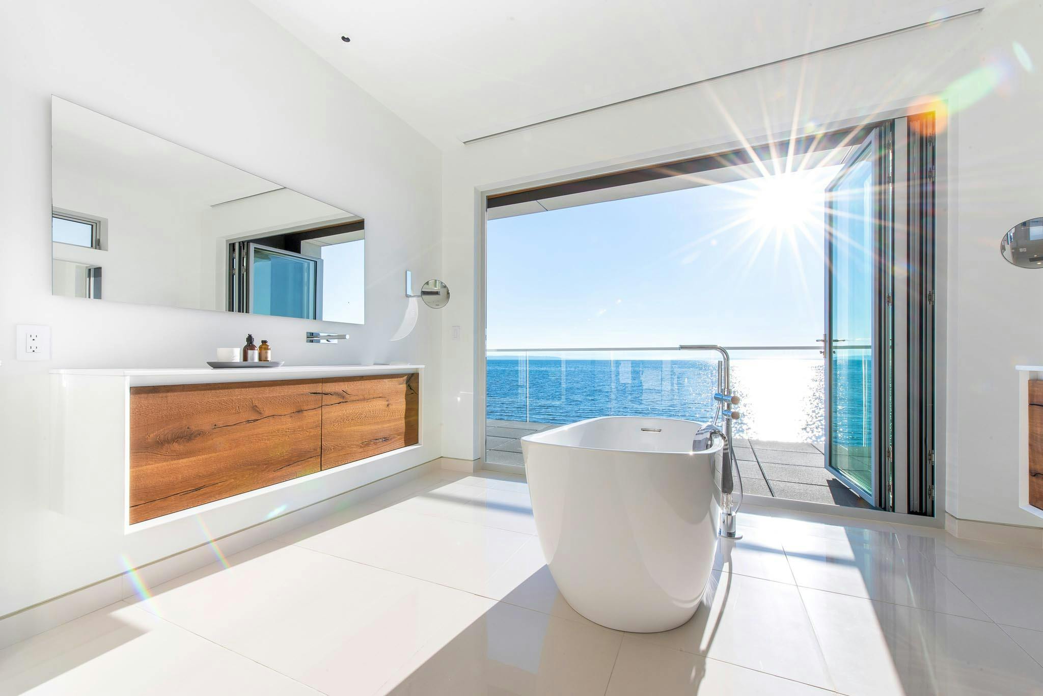 freestanding bathtub in front of open folding glass wall in oceanfront home